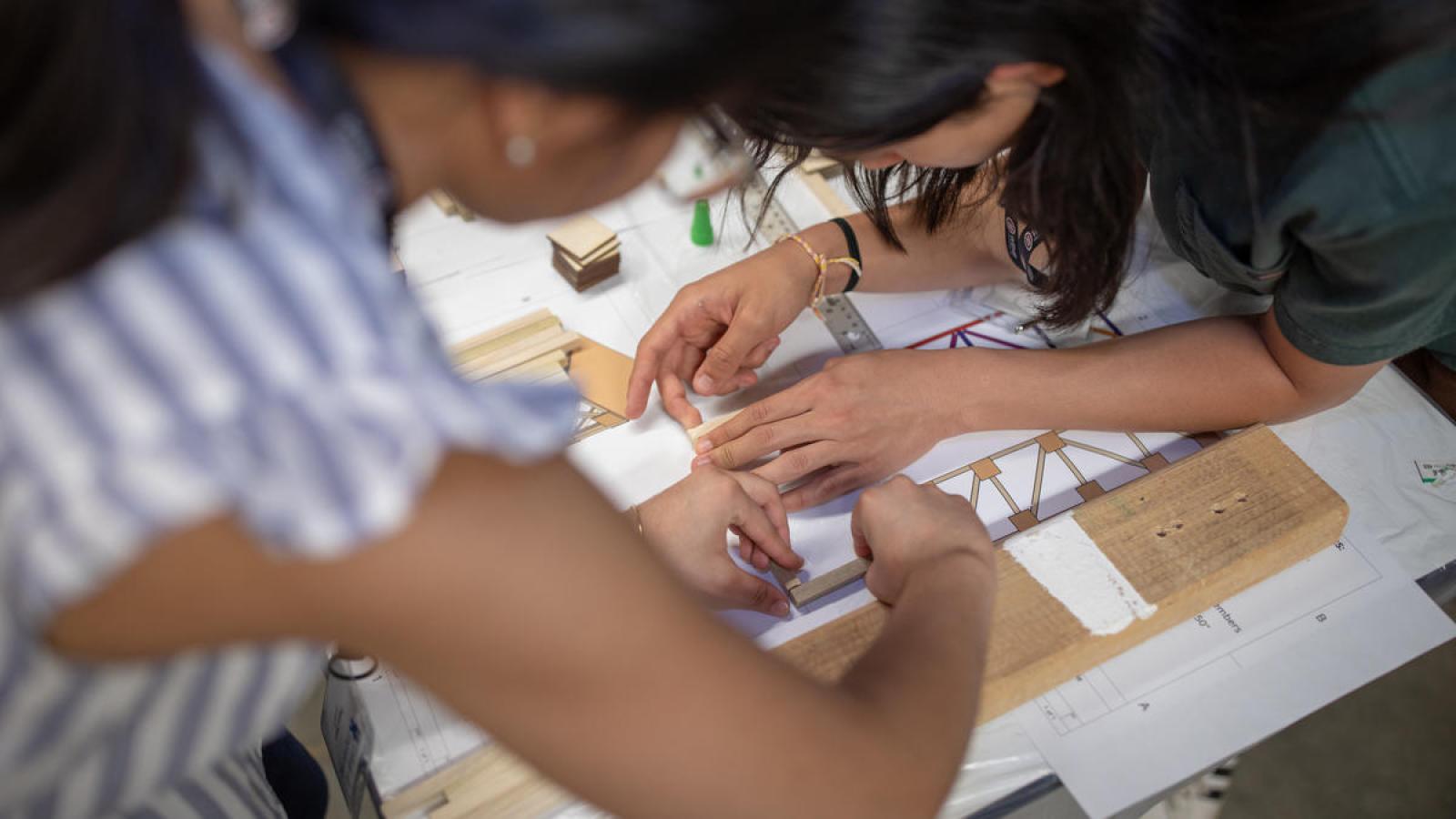 Two young women building a tower structure with wood craft materials.